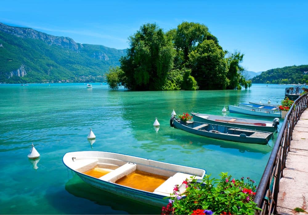 A nice Photo Lake Annecy on a calm day with boats in the foreground and a tree covered island.